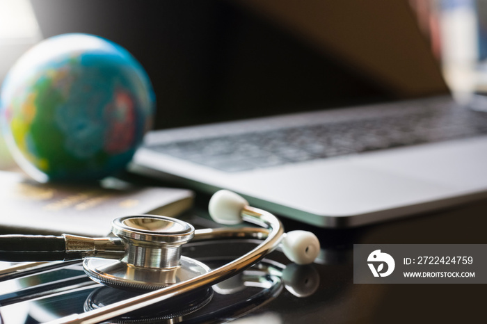 Blurred image of medical stethoscope, passport book, globe and laptop computer.Trip and Travel insurance concept.