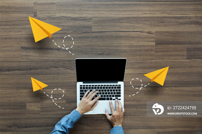 Top view businessman working on laptop computer PC with flying yellow paper airplanes