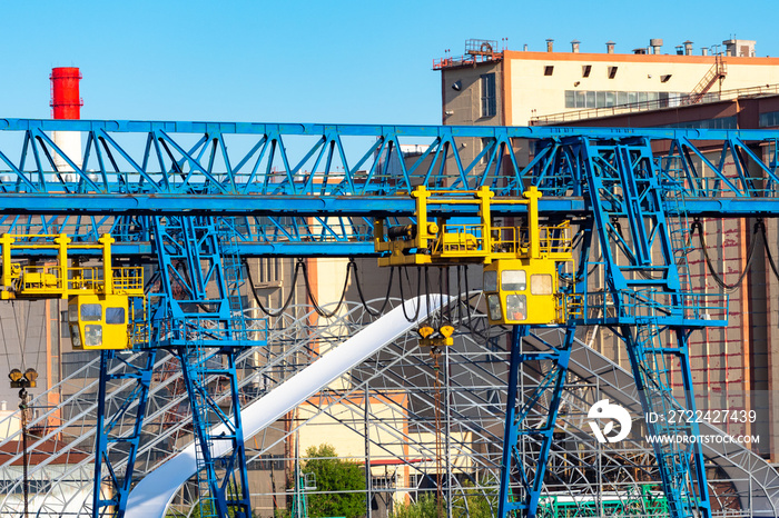 Overhead crane. Construction equipment on the background of buildings. A blue bridge crane next to an industrial building. Gantry crane. Special equipment for loading operations.