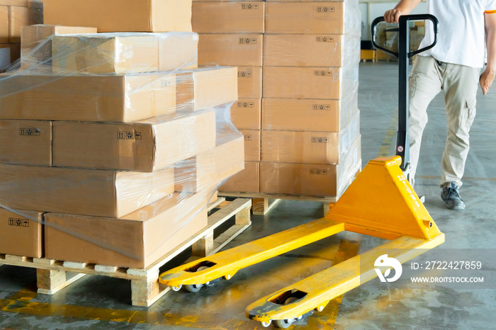 warehouse worker with yellow hand pallet truck or pallet jack hand lift, stack package boxes on wooden pallet at storage warehouse