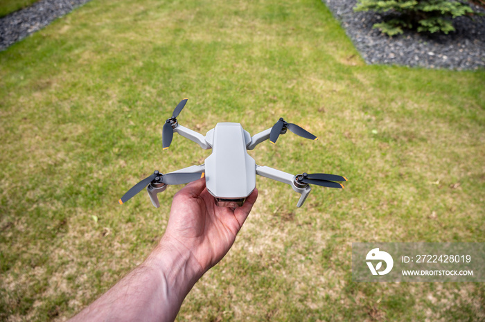 Male hand holding a small drone in a backyard.