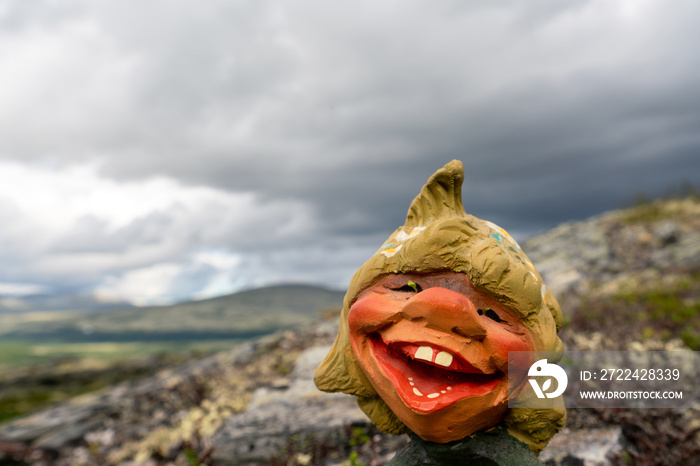 Funny Norwegian Troll figure laughing outdoors in dark and rainy landscape scenery.