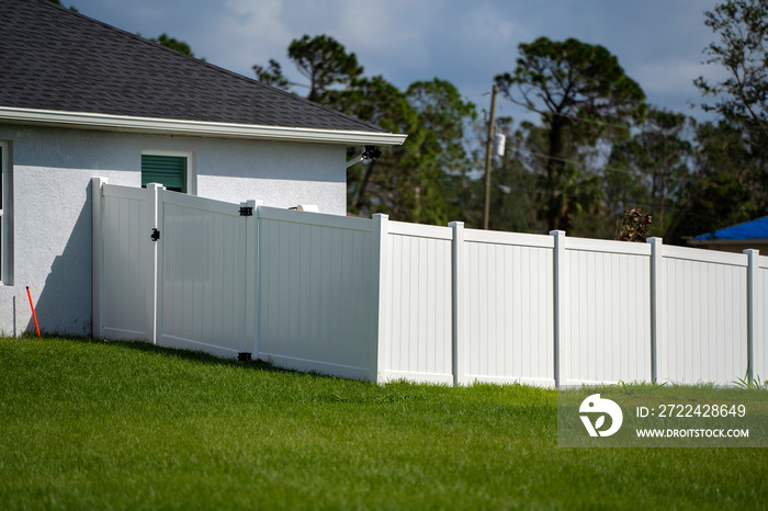 White vinyl picket fence on green lawn surrounding property grounds for backyard protection and privacy