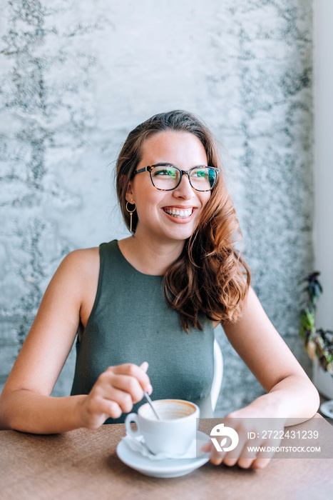 Beautiful young woman enjoying coffee cappuccino with foam near window.