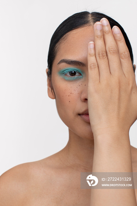 Woman wearing blue makeup, shielding part of face with hand