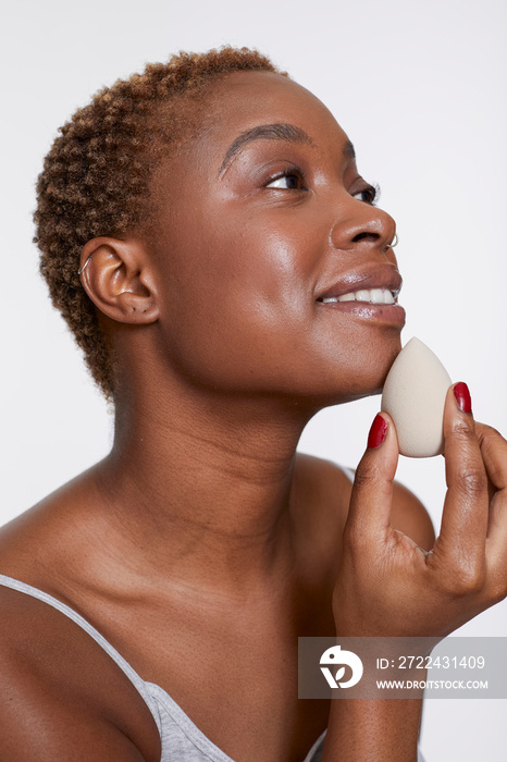 Studio portrait of smiling woman applying make up foundation with sponge