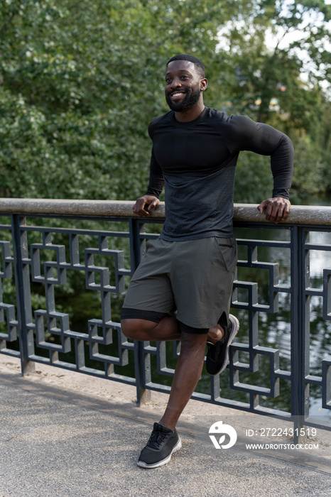 Portrait of smiling athletic man standing on footbridge in park