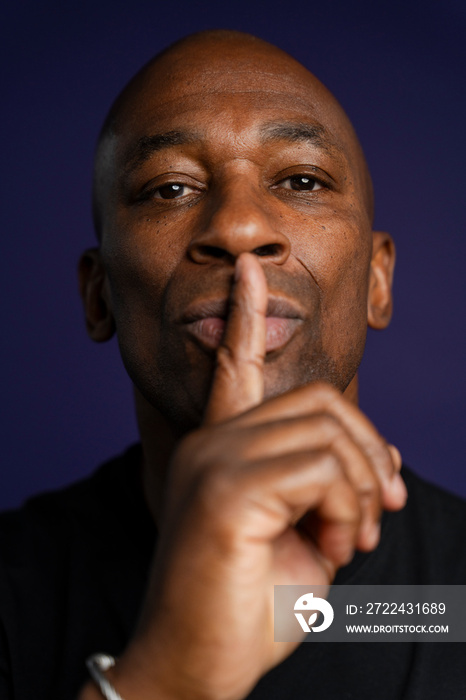 Portrait of man with finger on lips against purple background