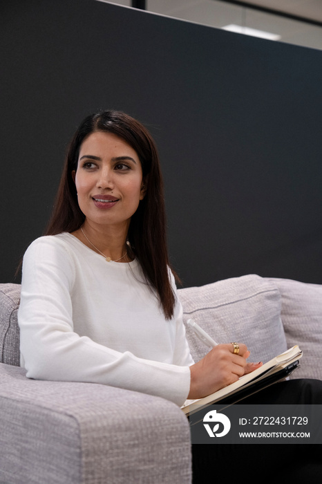 Woman sitting on sofa and writing in notepad