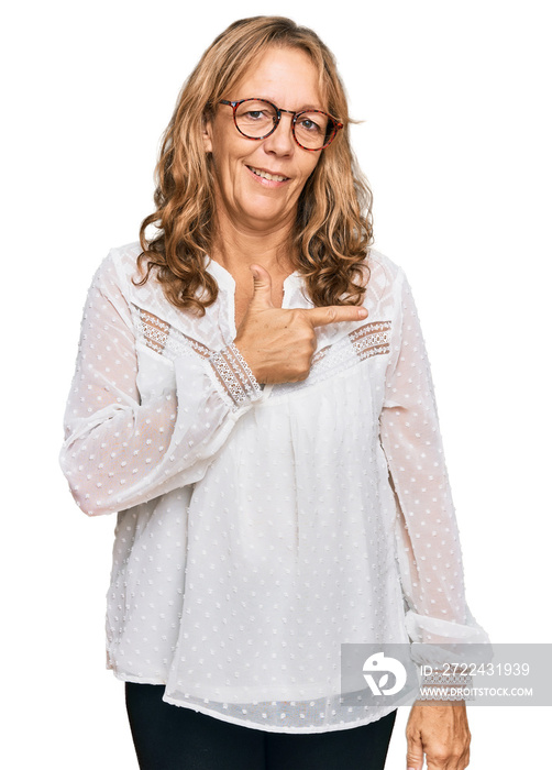 Middle age blonde woman wearing casual white shirt and glasses cheerful with a smile of face pointing with hand and finger up to the side with happy and natural expression on face