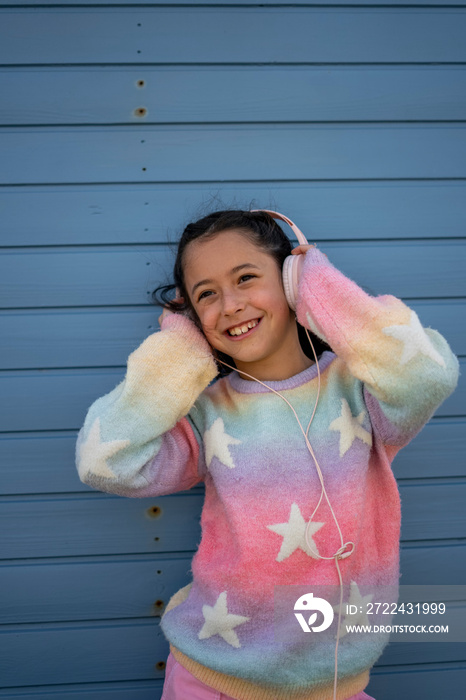 Smiling girl (8-9) in colorful clothes listening to music outdoors