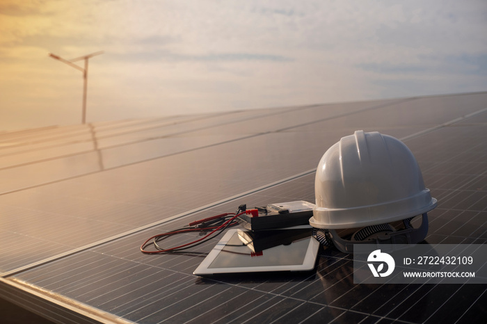 A white helmet, tablet and a voltmeter are placed on a solar panel against a sunlit background. alternative energy concept