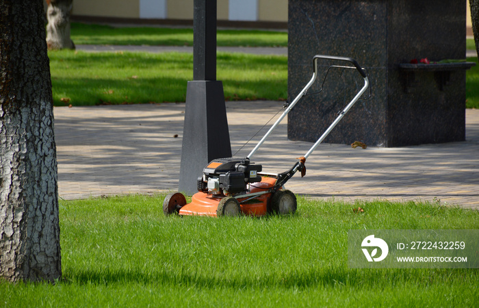 lawn mower stands on green grass. preparation for mowing the lawn. trimming of overgrown grass and ennoblement of the park area