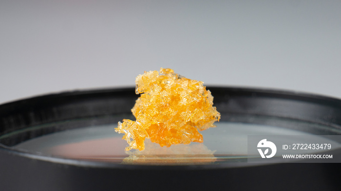 golden crystals of cannabis wax, glass container with crumbs of marijuana concentrate and copy space