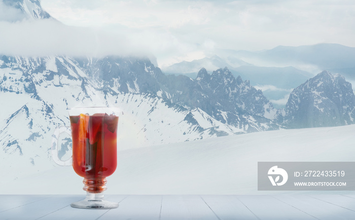 Mulled wine spiced and landscape of mountains on background. Alcohol hot drink in front of snowly mountains and cloudly sky. Warm in winter day, holidays, travel, New Year and Christmas time. .