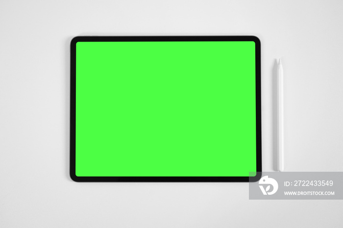 Mockup of tablet and digital pencil with pre-keyed green screen on white table.