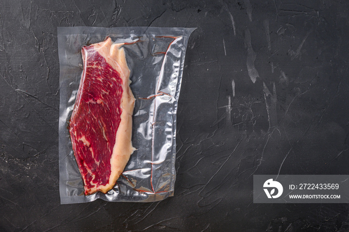 Picanha beef steak in vacuum sealed bag on black textured background, top view space for text.