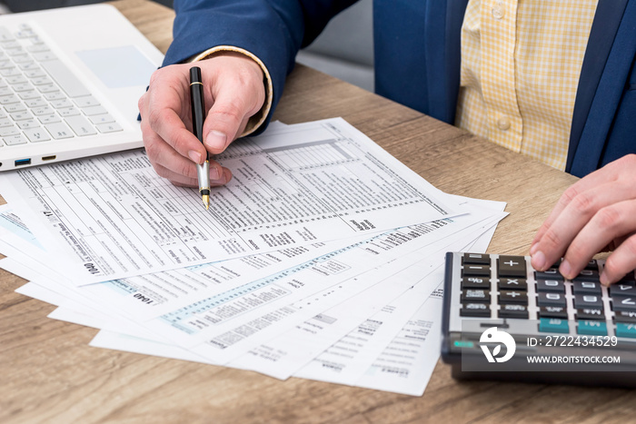 Businessman works with 1040 tax form, laptop and calculator