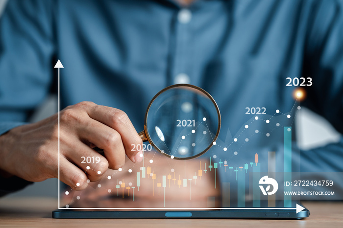 Businessman holding magnifier glass to focus increase analyze stock chart, forecast graph for trader searching the best business growth and profit earning stock market chart investment money concept.