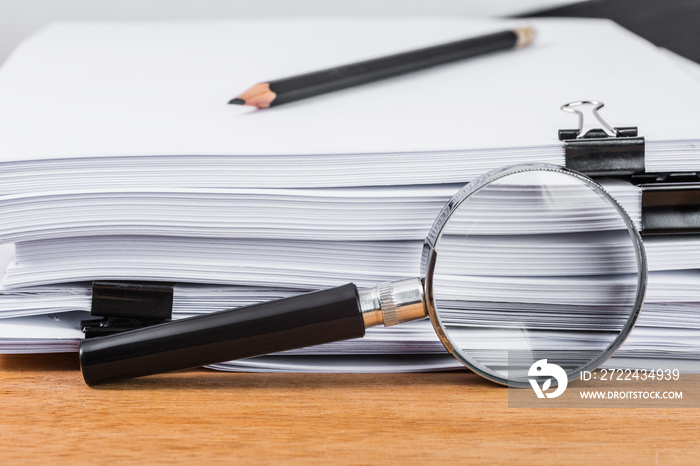 Close-up magnifying glass place on wooden table and search to edge of white documents