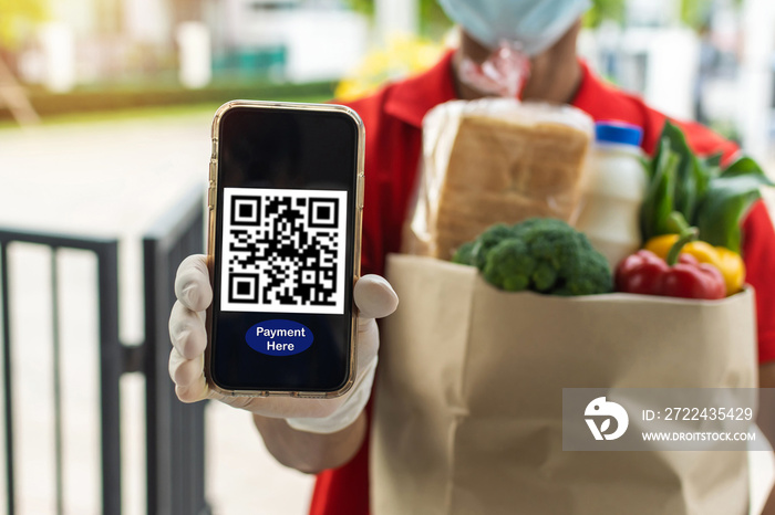 food delivery service man hand showing QR code on digital mobile phone and holding fresh food set bag waiting for customer at door home, digital payment technology and fast food delivery concept