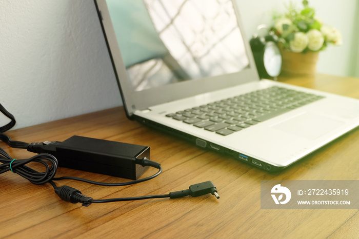 Plug in power outlet adapter cord charger on a white wall of the laptop computer on Wooden floor