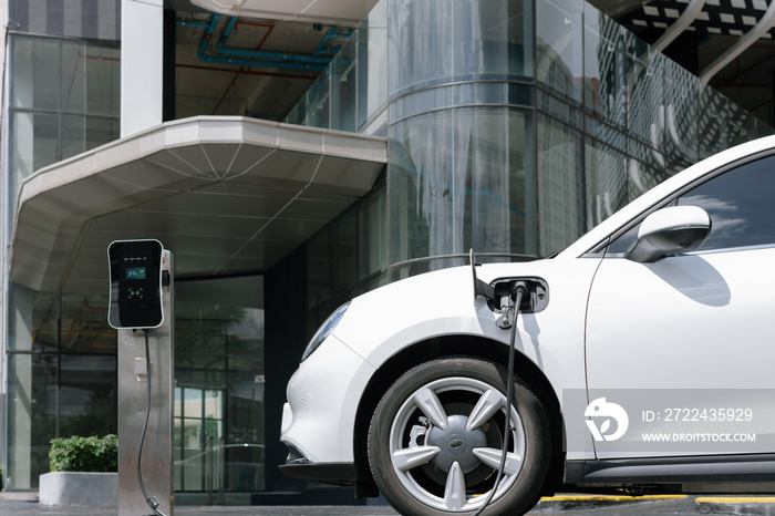 Progressive electric vehicle recharging battery at charging station powered by sustainable clean energy at city residential area. Eco-friendly vehicle concept.