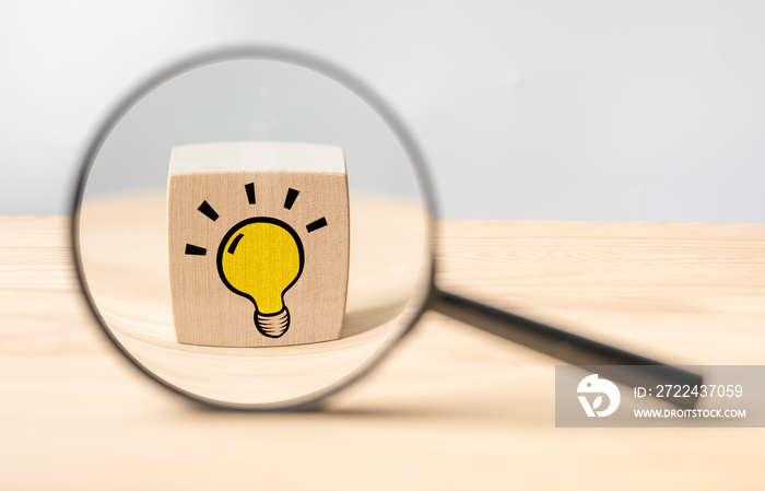 Magnifying glass with light bulb icon. Concept creative idea and innovation. Looking though magnifying glass onto lightbulb. Magnifying glass with light bulb on a wooden background