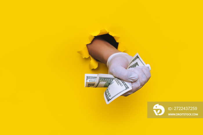 A doctor hand holds money (dollars) in white medical glove. Yellow torn hole paper background.The concept of treatment fees, bribes, illegal surgery. Copy space.