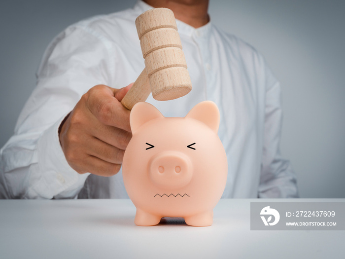 The pink piggy bank makes fear with afraid face while businessman man hand is holding a wooden hammer to smashing for getting the money on table and white background.