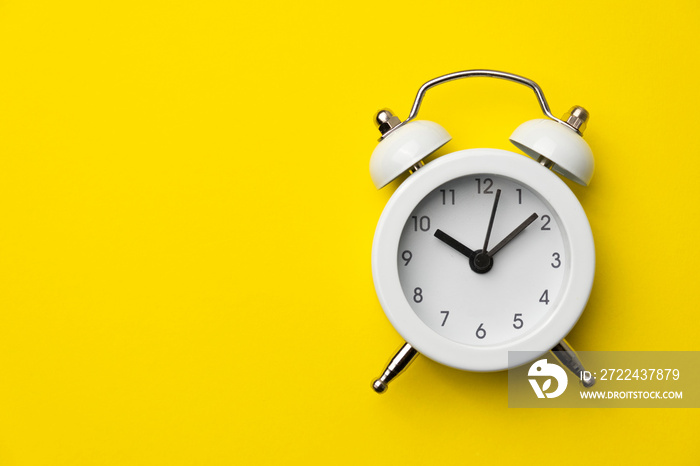 White analog alarm clock isolated on yellow background. Concept of time management. Copy space. Close-up.