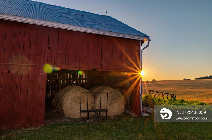 Red Barn at Sunset with Stored Round Hay Bails Inside and Wheat Field in Background