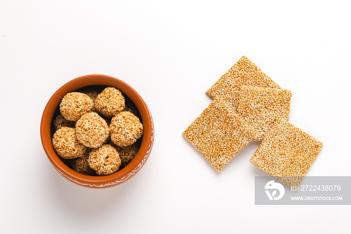 Til chikki and sesame seed ball on white background is an Indian sweet dish made with jaggery and sesame seeds.