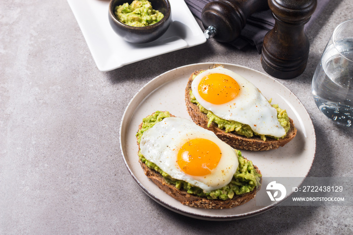 Avocado egg sandwich with a glass of water. Healthy light breakfast concept. Whole grain toasts with mashed avocado and fried eggs