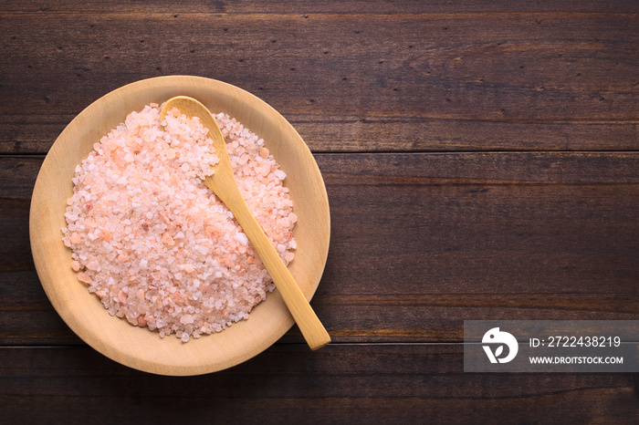 Coarse pink Himalayan salt on wooden plate with wooden spoon, photographed overhead with copy space on the side