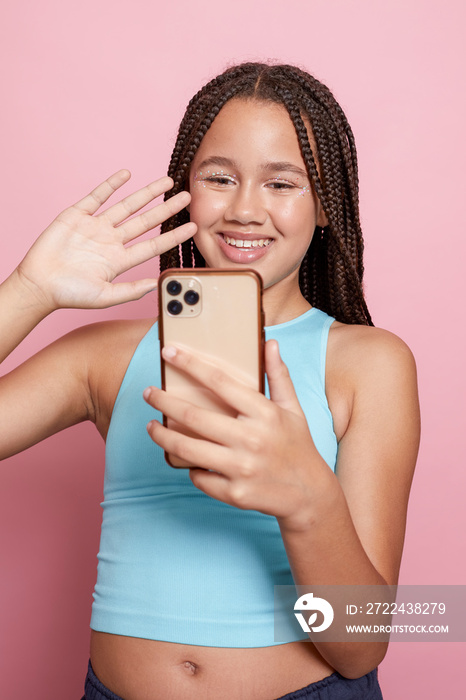 Studio shot of smiling girl with braids looking at smart phone