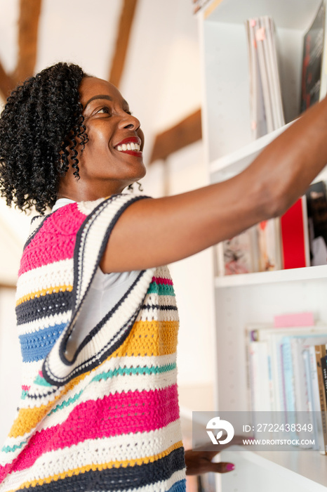 Smiling woman choosing book from shelf at home