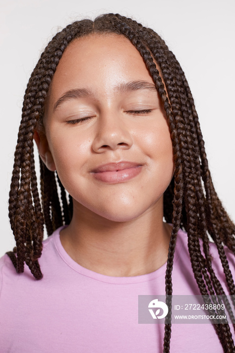 Studio portrait of smiling girl with braided hair and eyes closed