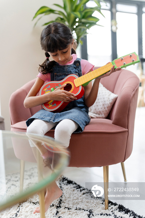 Little girl playing on ukulele in living room