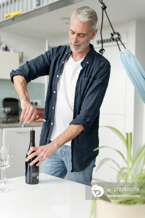 Mature man opening red wine at home