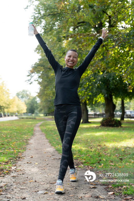 Portrait of smiling athletic woman with arms raised in park