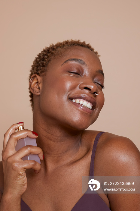 Studio portrait of smiling woman spraying perfume on neck