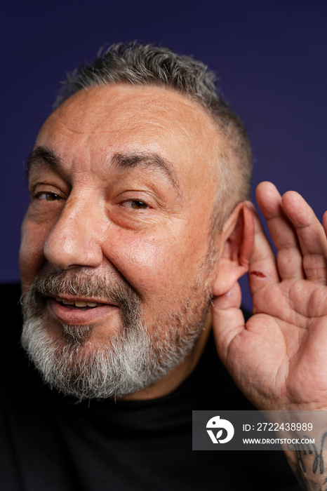 Portrait of smiling man with hand on ear against purple background