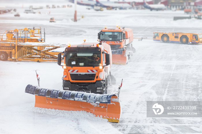 Snowplow removing snow from runways and roads in airport during snow storm, view through window