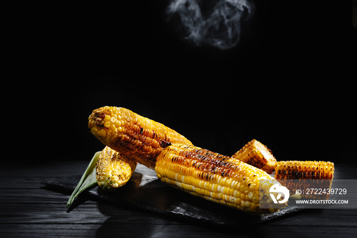 Grilled corn with smoke. A cob of corn roasted over charcoal on a wooden board. Whole corn cobs.