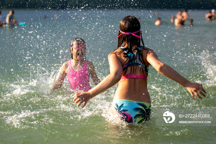 Girls having fun in lake splashing water on summer sunny hot day outdoors