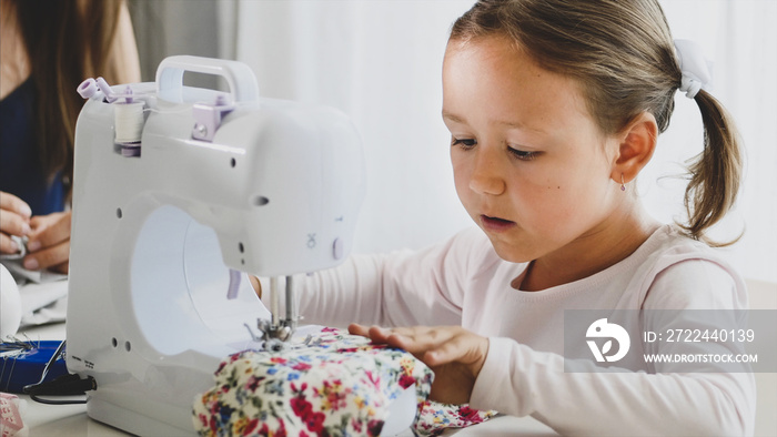 Mother and daughter is sewing on a machine. Portrait of daughter with mother on the background. A mother and a daughter are spending time at home together, day time.