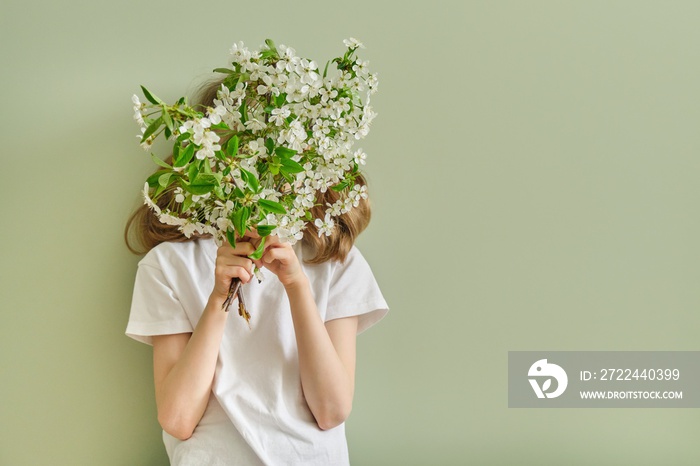 Girl child with spring white flowers blooming cherry branches, green wall background, copy space