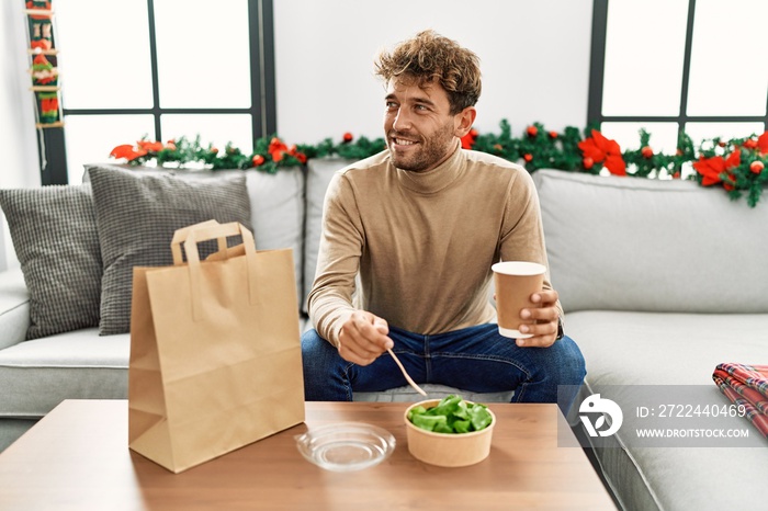 Young hispanic man eating take away salad sitting by christmas decor at home