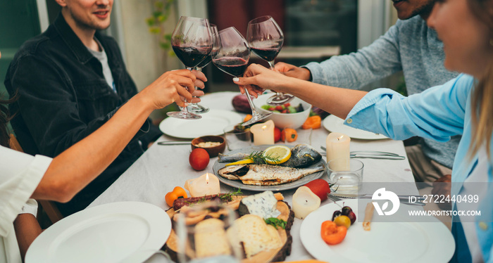 Group of people toasting with red wine glasses during dinner party at rooftop, Summer Weekend Celebration Concept, Happy friends celebrating birthday enjoying time together making cheers with red wine